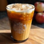 A Starbucks Pumpkin Spice Latte with ice and cinnamon topping, in a Starbucks branded glass.