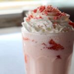 Close-up of a pink strawberry Starbucks drink topped with whipped cream and red sprinkles.