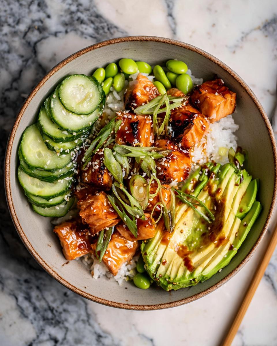 Overhead view of a Teriyaki Salmon Bowls featuring glazed salmon cubes over rice with avocado, cucumbers, and edamame.