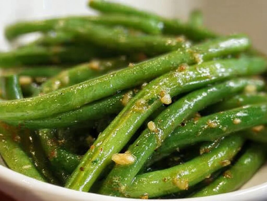 Close-up of bright green Thanksgiving green beans tossed with garlic and seasoning in a white bowl.