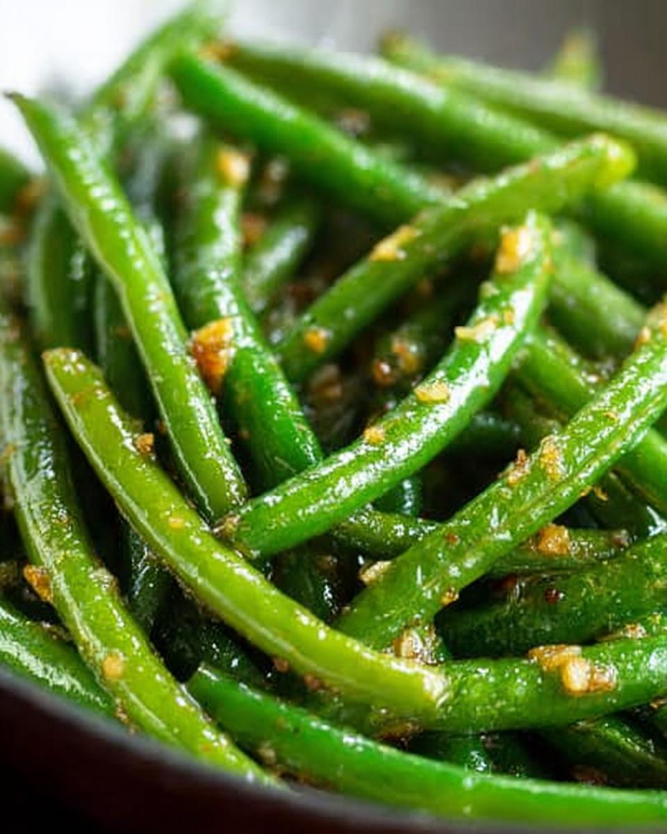 Close-up of glistening, perfectly cooked Thanksgiving green beans with garlic and seasoning.