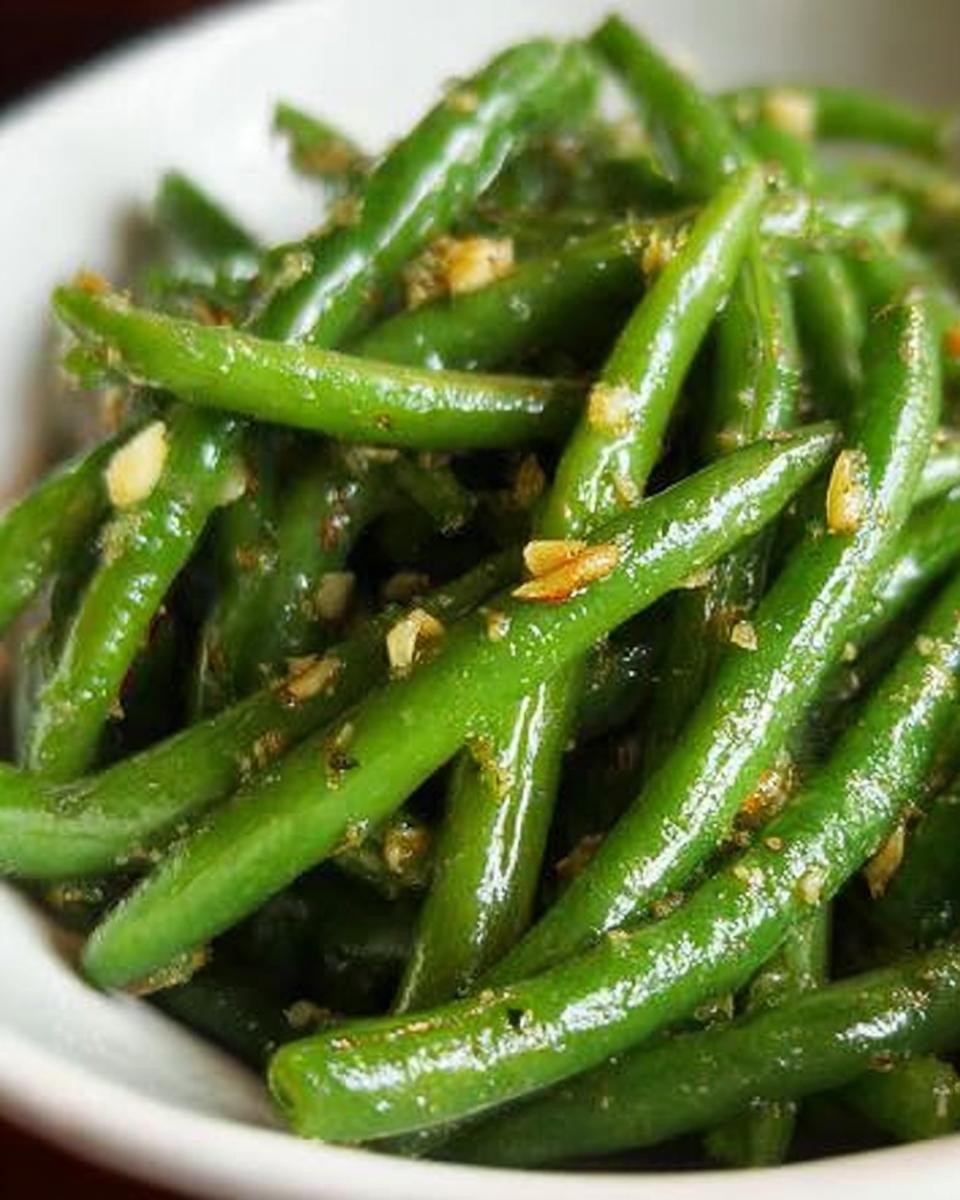 Close-up of glossy, perfectly cooked Thanksgiving green beans tossed with minced garlic and seasonings.