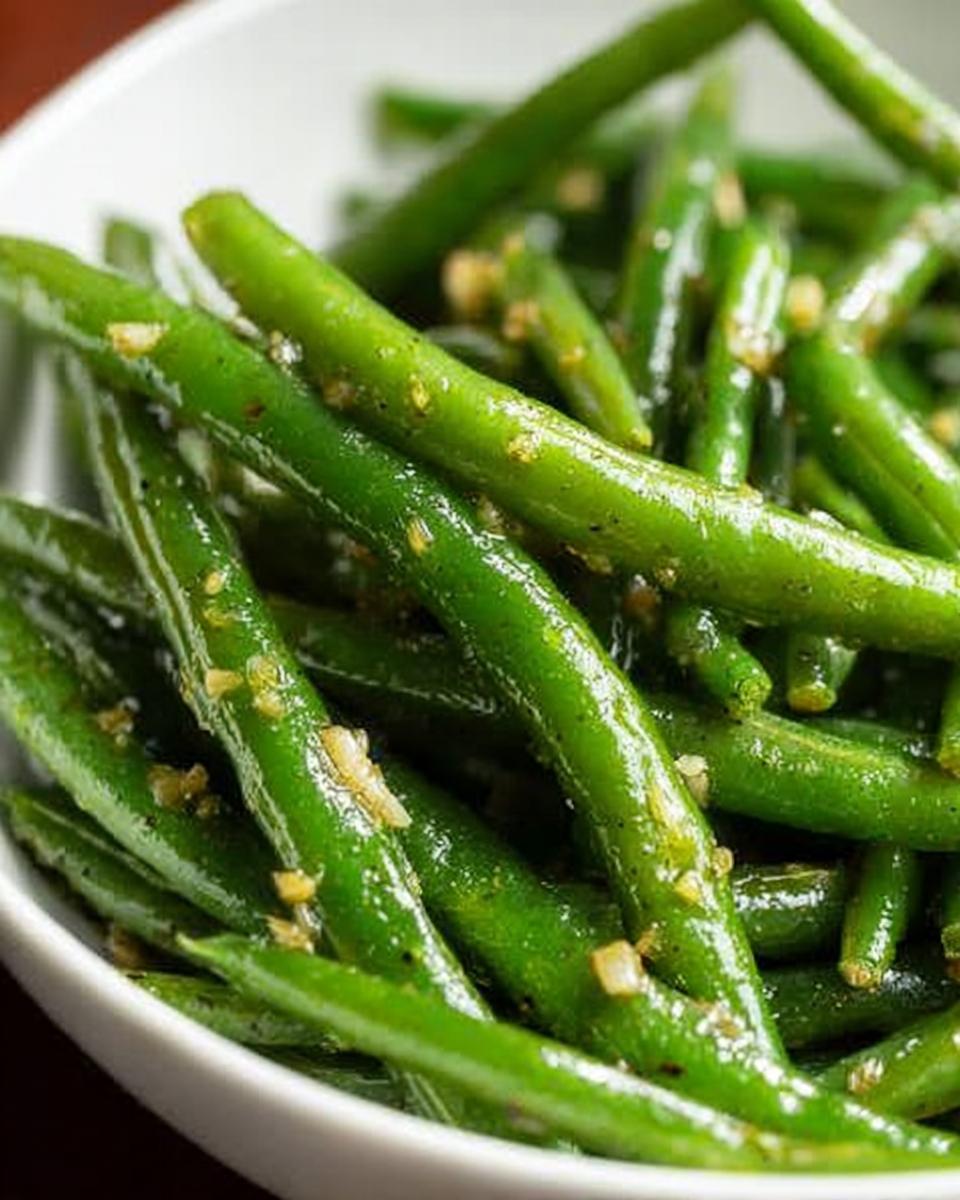 Close-up of bright green Thanksgiving green beans tossed with minced garlic in a white bowl.