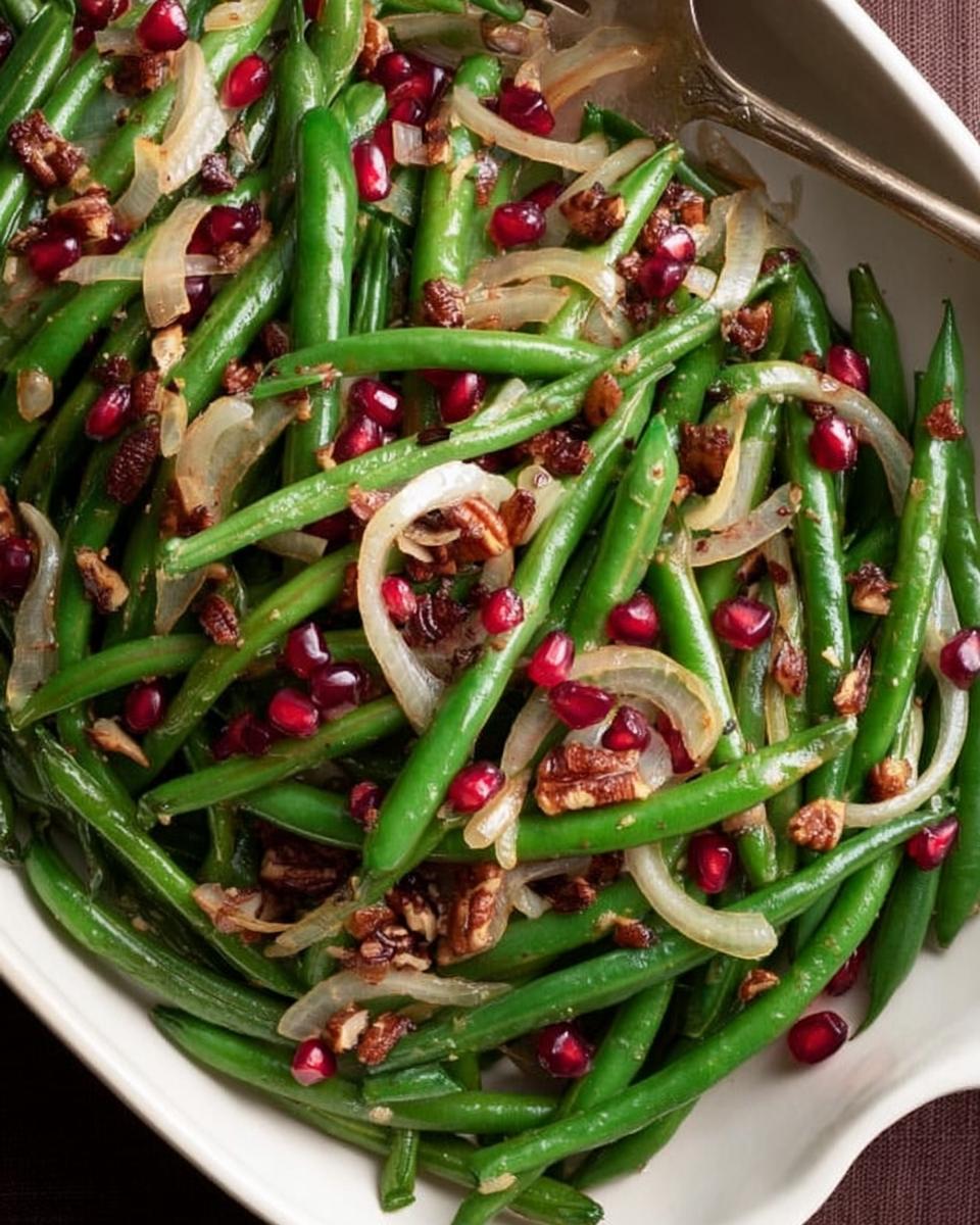 Close-up of vibrant Thanksgiving green beans tossed with caramelized onions, ruby-red pomegranate seeds, and crunchy pecans.
