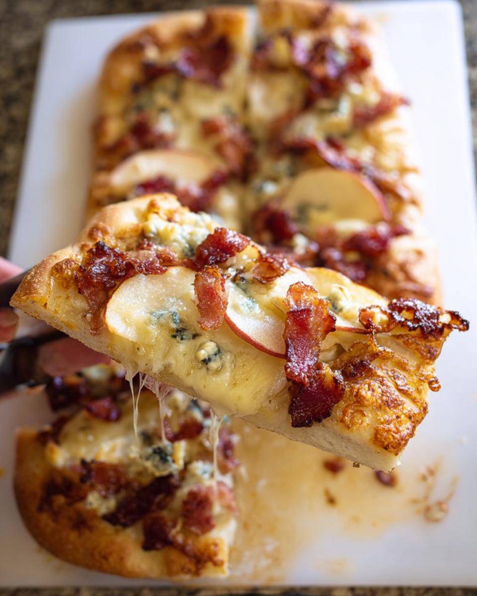 A slice of 10-ingredient pizza with bacon, apple, and blue cheese being lifted, showing melted cheese.