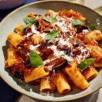 A close-up of rigatoni pasta with a rich tomato sauce, chunks of eggplant, and topped with grated cheese and fresh basil. This is one of the 12-Ingredient Pasta Recipes.