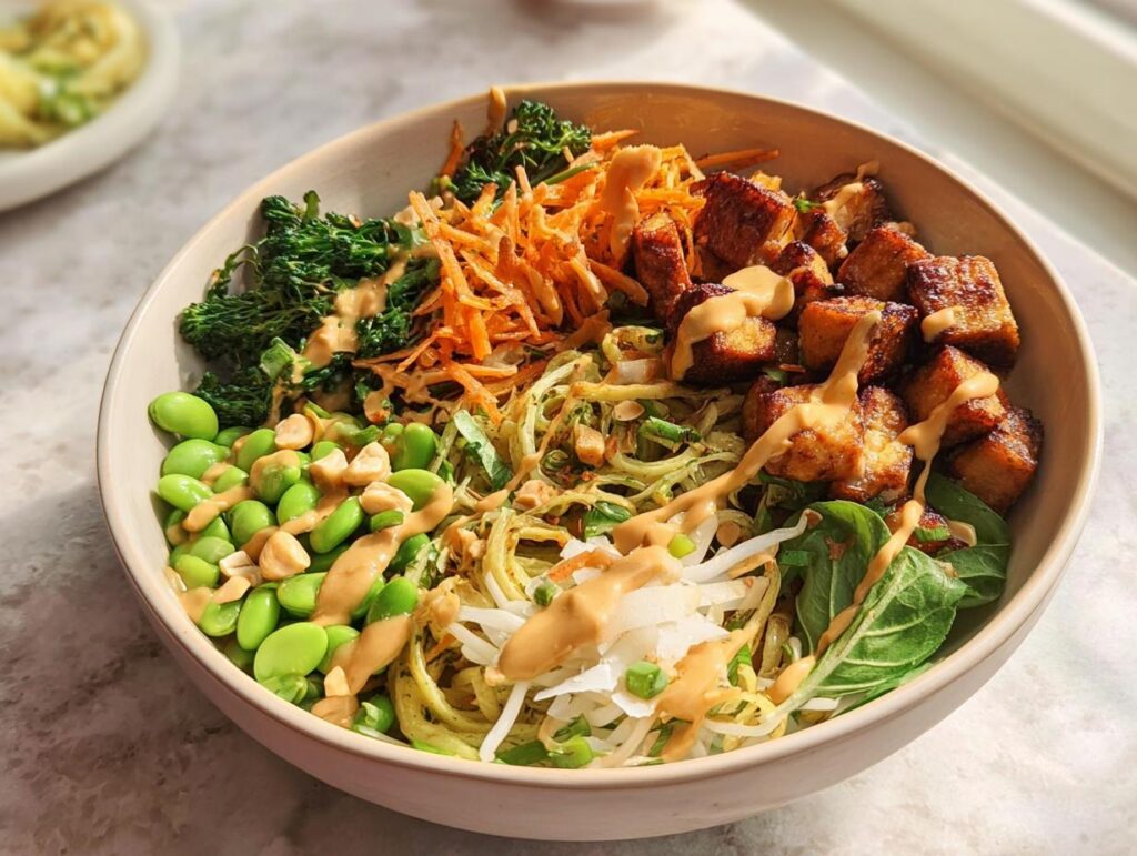 A vibrant and healthy 20-ingredient rice bowl filled with edamame, tofu, shredded carrots, and greens, drizzled with a creamy sauce.