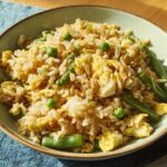 A bowl of 7-ingredient egg fried rice featuring scrambled egg, green beans, and peas.
