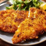 Two golden-brown, crispy air fryer chicken breasts served with a side of salad and a lemon wedge.