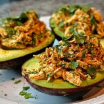 Two avocado halves filled with seasoned chicken salad and topped with fresh parsley and paprika. A quick and easy sandwich idea.