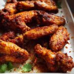 Close-up of a platter of perfectly baked chicken wings, coated in a savory spice rub.