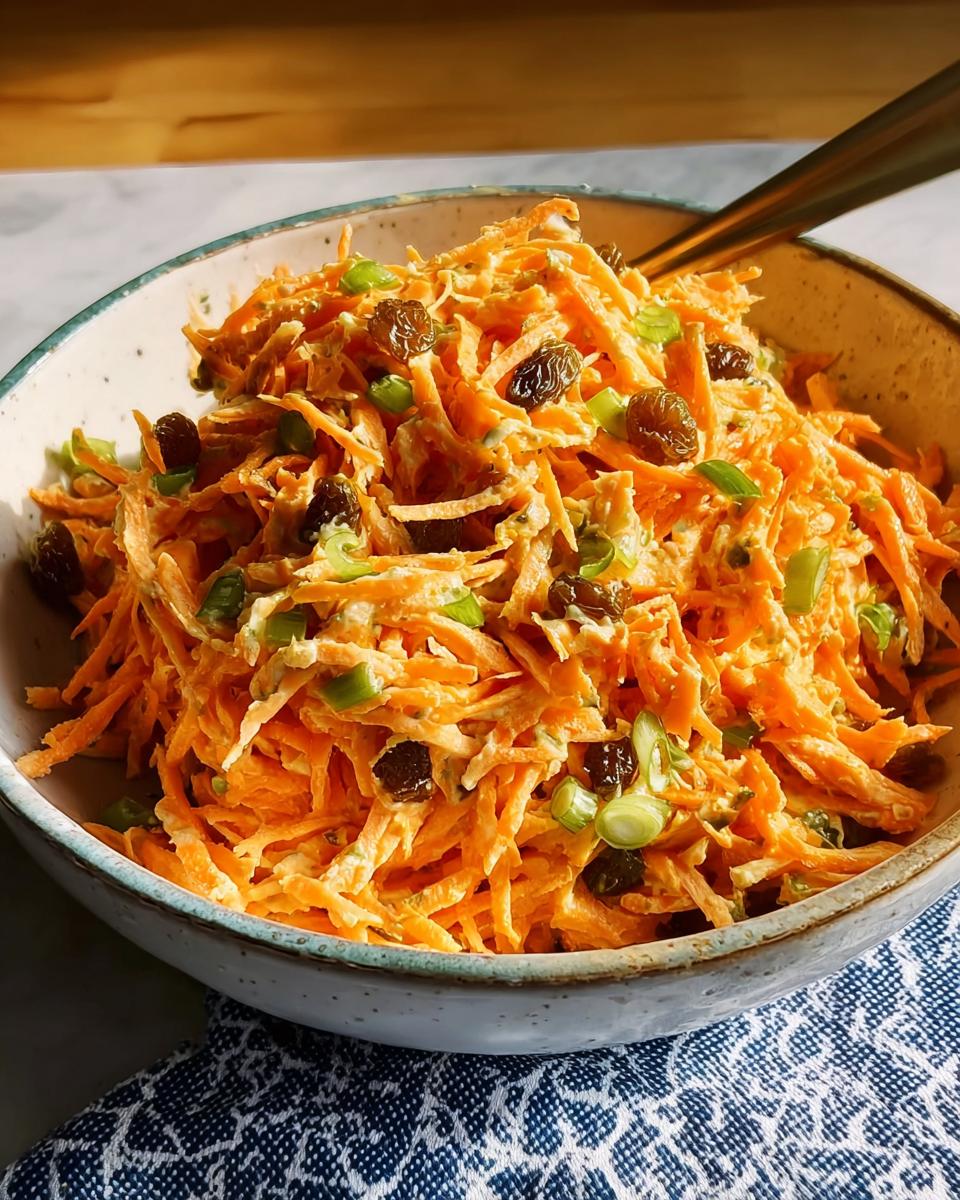 A bowl of shredded carrot salad with raisins and green onions, perfect for quick veggie sides recipes.
