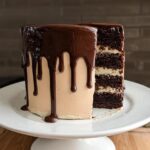A slice of rich chocolate cake with creamy frosting and chocolate ganache drip, showcasing layers of cake and filling.