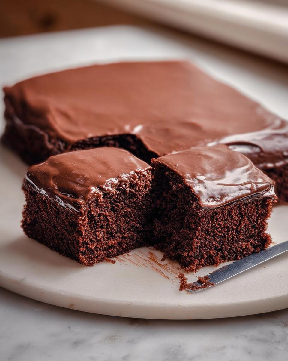 Close-up of a rich chocolate cake with glossy frosting, cut into two pieces, showcasing its moist crumb.
