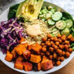 A vibrant and healthy rice bowl recipe featuring quinoa, roasted sweet potatoes, chickpeas, red cabbage, cucumber, avocado, and a creamy dressing.