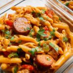 Close-up of creamy sausage pasta in a meal prep container, featuring penne pasta, sliced sausage, bell peppers, and parsley.