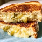 A close-up of a dill pickle grilled cheese sandwich, showing gooey melted cheese and pickle slices.