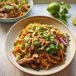 A close-up of a bowl of Pad Thai noodles with beef, peanuts, cilantro, and lime, perfect for easy dinner recipes.