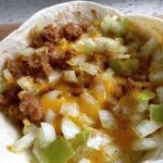 Close-up of a breakfast taco filling with crumbled sausage, diced onions, green peppers, and melted cheese.