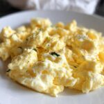 Close-up of fluffy scrambled eggs seasoned with black pepper and herbs on a white plate.
