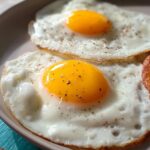 Two perfectly fried eggs with runny yolks, seasoned with pepper, served with hash browns.