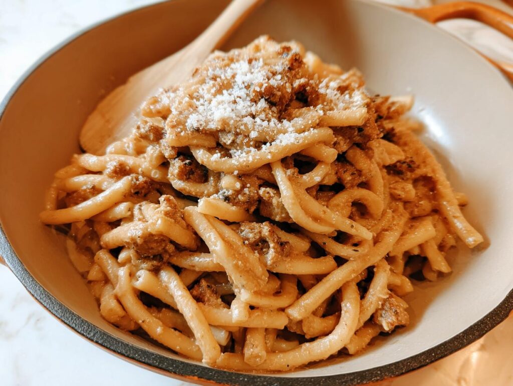 Close-up of a bowl of thick pasta with a rich sauce and crumbled meat, topped with grated cheese. One of 20 genius pasta recipes ideas for busy weeknights.