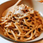 Close-up of a bowl of thick pasta with a rich sauce and crumbled meat, topped with grated cheese. One of 20 genius pasta recipes ideas for busy weeknights.
