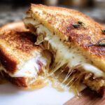 A close-up of a perfectly grilled cheese sandwich, oozing with melted cheese and caramelized onions.