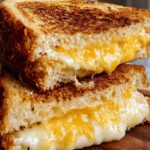 A stack of two golden-brown grilled cheese sandwiches, oozing with melted cheese.