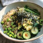 A vibrant rice bowl featuring brown rice, sliced avocado, edamame, cucumber, nori, and sesame seeds.