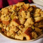 A close-up of a bowl filled with homemade stuffing, featuring chunks of bread, celery, and herbs.