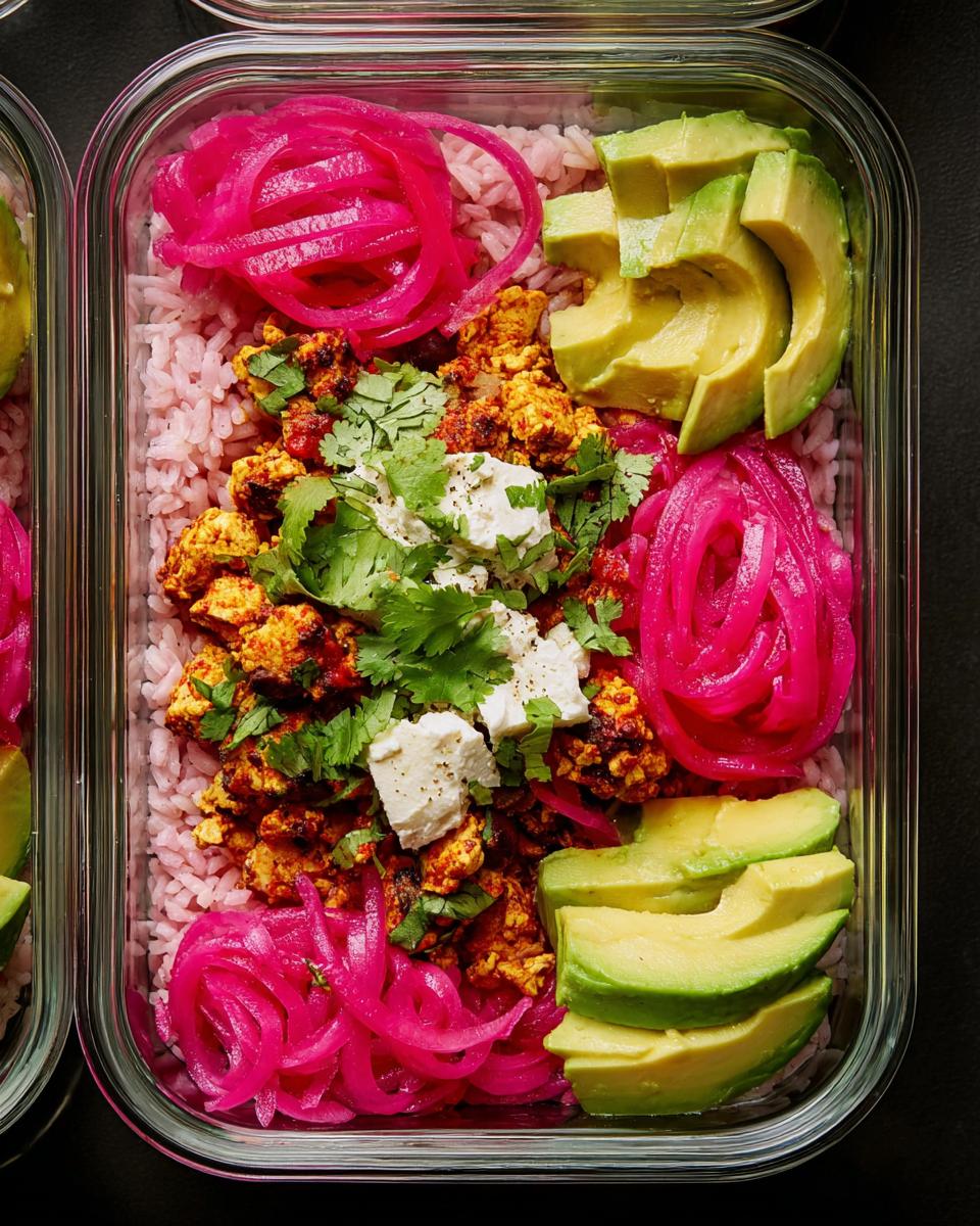 Overhead view of a meal prep container filled with pink rice, seasoned tofu, sliced avocado, and pickled red onions.