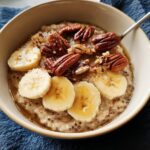 A bowl of oatmeal topped with sliced bananas, pecans, and drizzled with honey, perfect for busy weeknight breakfast ideas.