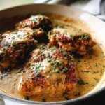 Four pan-seared chicken thighs in a creamy sauce, garnished with fresh chives, a perfect beginner chicken thigh recipe.
