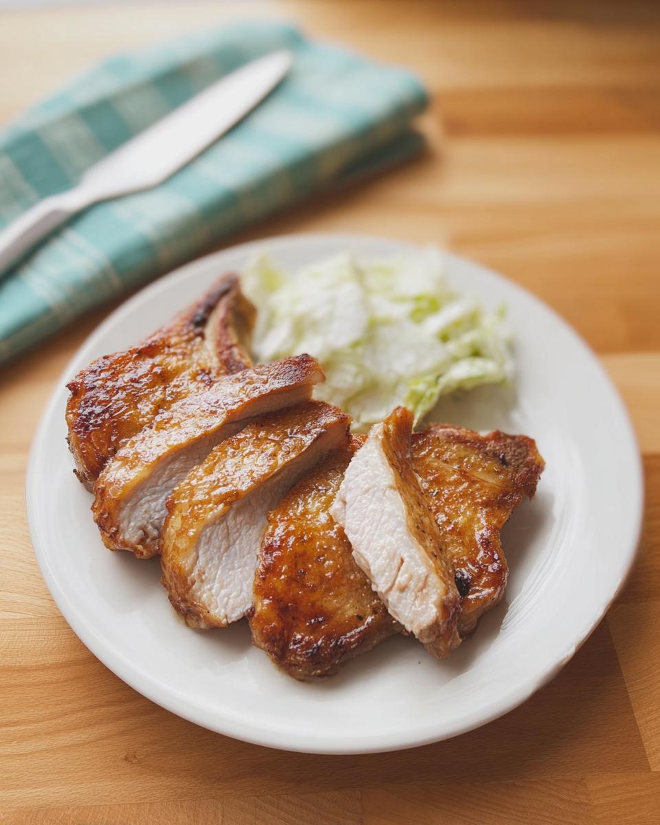 A plate of perfectly cooked, juicy pork chops, sliced and served with a side of shredded lettuce.