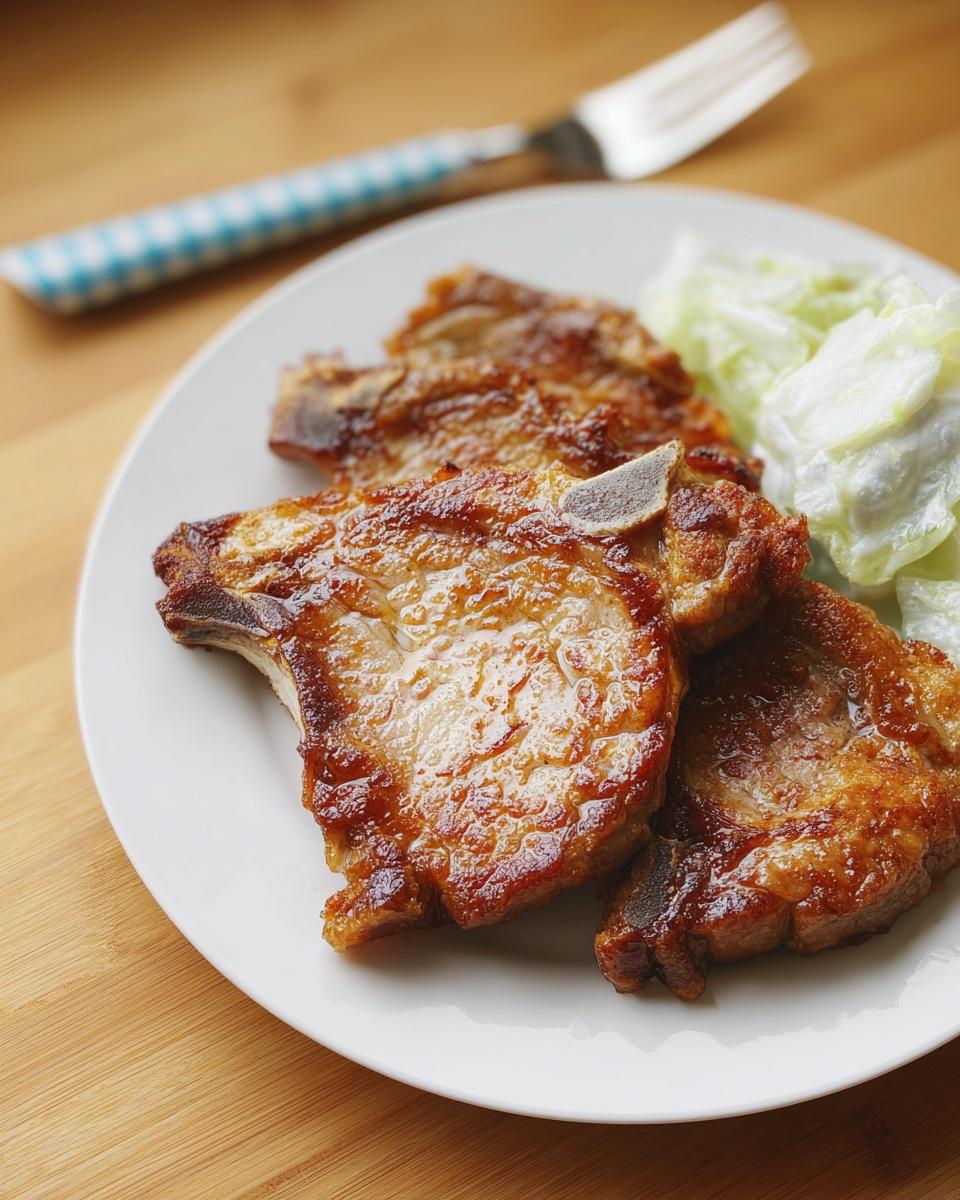 Close-up of three juicy, pan-seared pork chops with a glaze, served with a side of coleslaw.