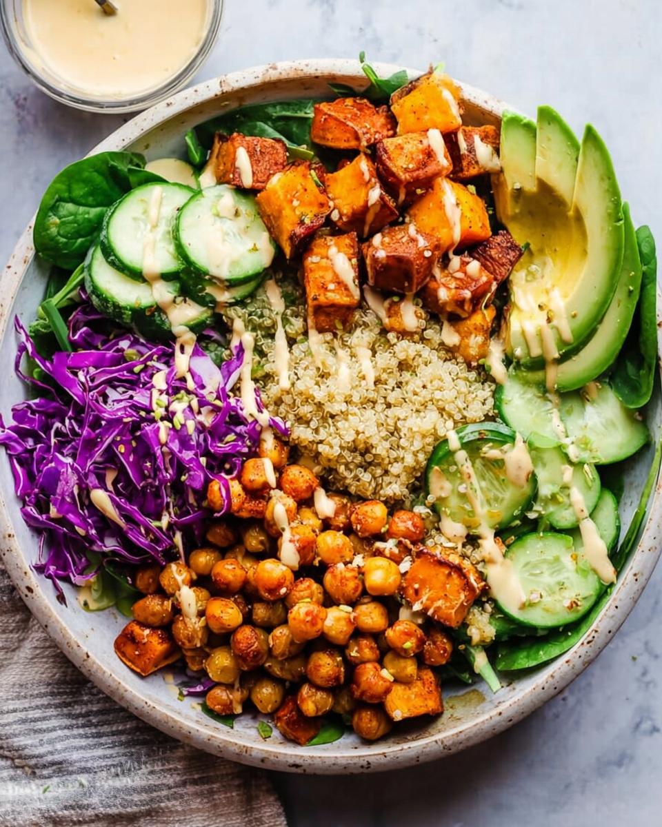 A vibrant and healthy quinoa rice bowl recipe featuring roasted sweet potatoes, chickpeas, avocado, cucumber, red cabbage, and spinach with a creamy dressing.