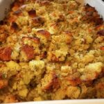 Close-up of a baked restaurant-style stuffing recipe at home, featuring golden-brown bread cubes and visible vegetables.