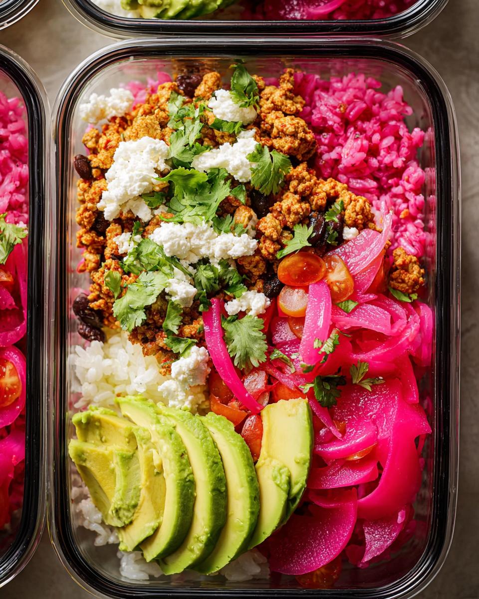 Overhead view of a meal prep container filled with rice bowls recipes: seasoned ground meat, white rice, pink rice, pickled onions, and crumbled feta cheese.