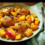 A plate of roasted chicken thighs served with cubes of butternut squash and apple slices, garnished with rosemary.