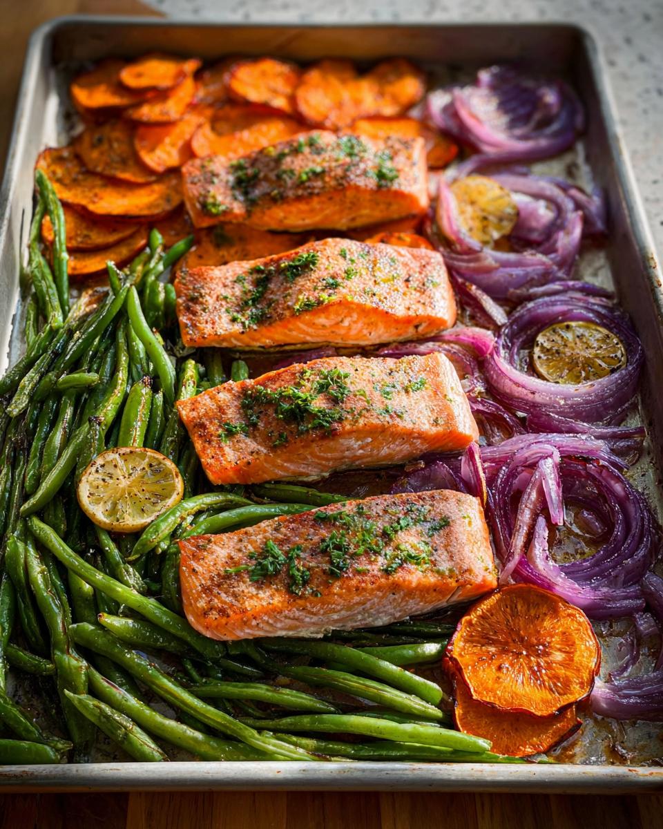 Four salmon fillets baked on a sheet pan with green beans, sweet potato slices, and red onion for meal prep.