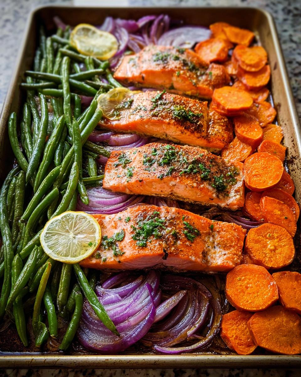 Four salmon fillets baked on a sheet pan with green beans, red onions, and sweet potatoes, perfect for salmon recipes meal prep.