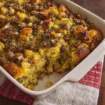 A close-up of a baking dish filled with savory sausage cornbread stuffing, garnished with fresh herbs.