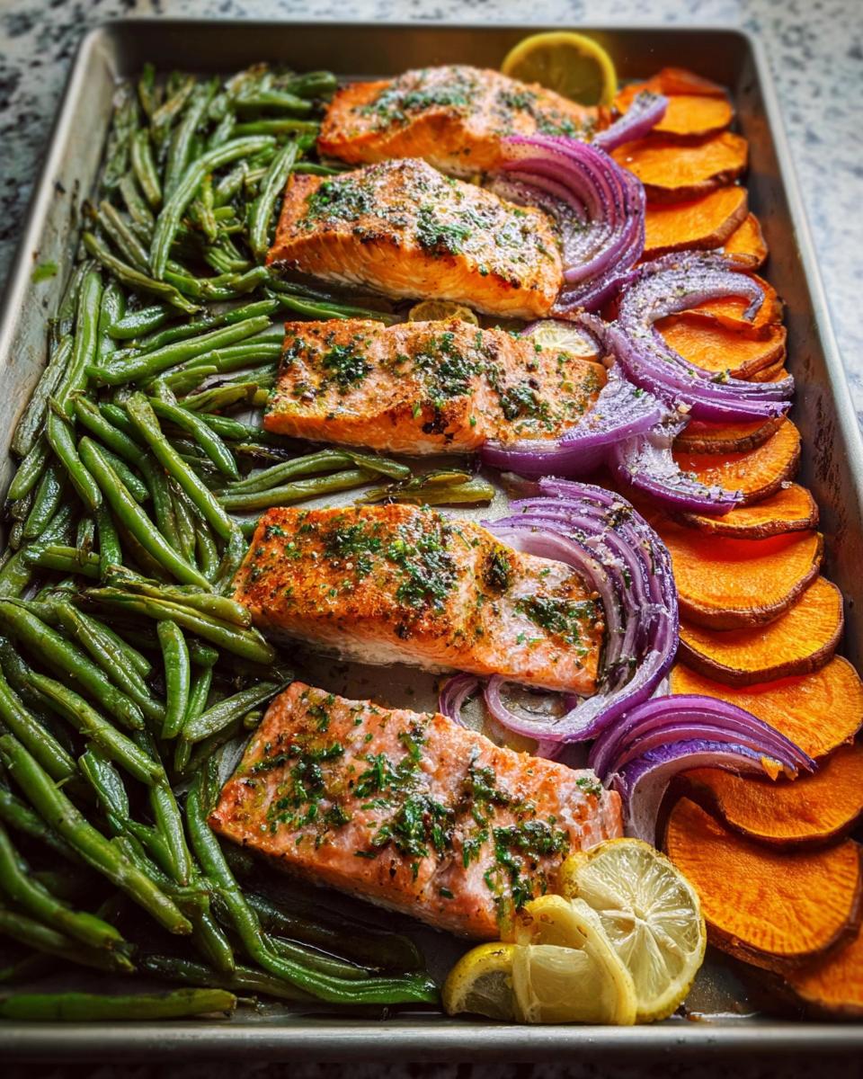 Sheet pan meal prep with seasoned salmon fillets, green beans, sweet potato slices, and red onion wedges.
