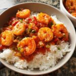 A bowl of fluffy white rice topped with a flavorful shrimp and tomato sauce, perfect for shrimp recipes.