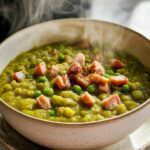 A steaming bowl of split pea soup with chunks of ham and whole peas, perfect for learning how to make soup recipes.
