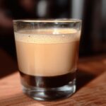 A layered Starbucks drink recipe idea in a shot glass, featuring dark espresso at the bottom and creamy frothed milk on top.