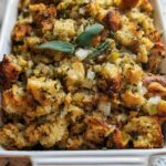Close-up of a white baking dish filled with homemade stuffing, featuring toasted bread cubes, onions, celery, and herbs.