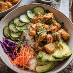 A close-up of a vibrant Bang Bang Chicken Bowl, featuring crispy chicken, rice, avocado, cucumber, and shredded carrots.
