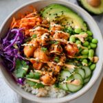 A vibrant bowl of Bang Bang Salmon Bites Bowls, featuring crispy salmon, rice, avocado, edamame, cucumber, and shredded carrots.
